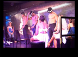 Female bachelorette sitting on a chair on stage at the male strip show while the strippers dance for them.